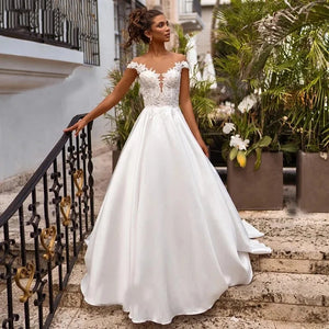 Elevate your wedding day look with the Robe Joanne. Featuring delicate lace appliques, modern satin fabric, and elegant cap sleeves, this dress offers a timeless and sophisticated style for any bride. Say "I do" in comfort and confidence with this stunning and versatile wedding dress.