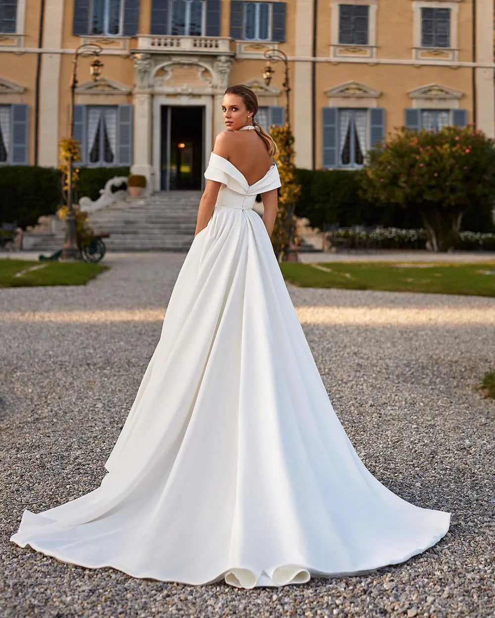 Indulge in luxury on your special day with the Robe Lotta. Featuring an elegant white A-line design and an off-the-shoulder neckline, this wedding dress is made of smooth satin for a sophisticated look and feel. Make a statement that exudes grace and refinement with this exclusive piece.