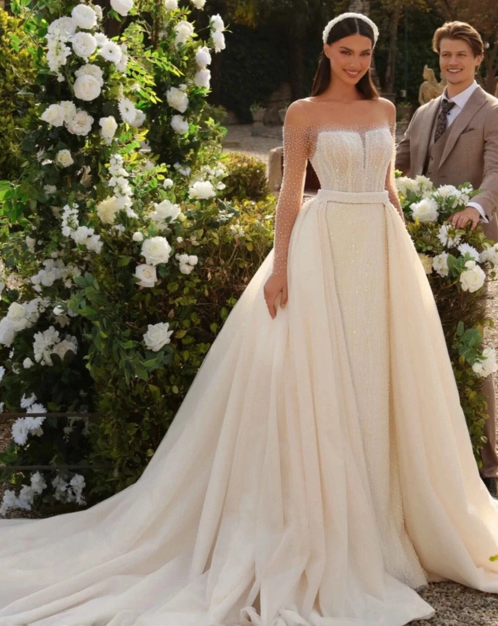 Indulge in luxury with our Robe Amaris, a classic O-neck wedding dress that exudes elegance and sophistication. Adorned with sparkly sequins and beads, this mermaid style gown features a detachable train for added drama. Make a statement on your special day with this exclusive piece.