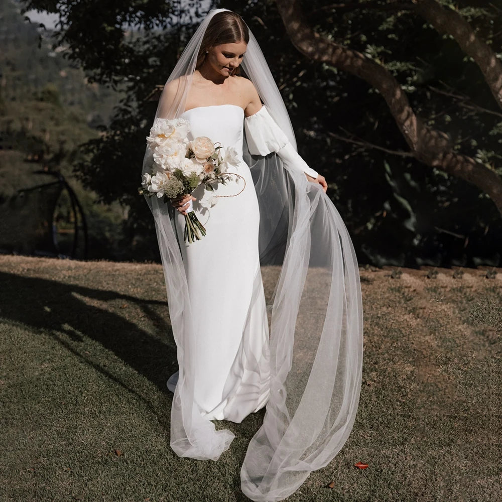 Introducing the Robe Eglantine, a minimalist wedding dress that exudes effortless elegance. This ivory crepe gown features detachable long sleeves for versatility and a sleek sheath silhouette with a brush train for a modern touch. The strapless design and buttons closure add convenience for the bride.