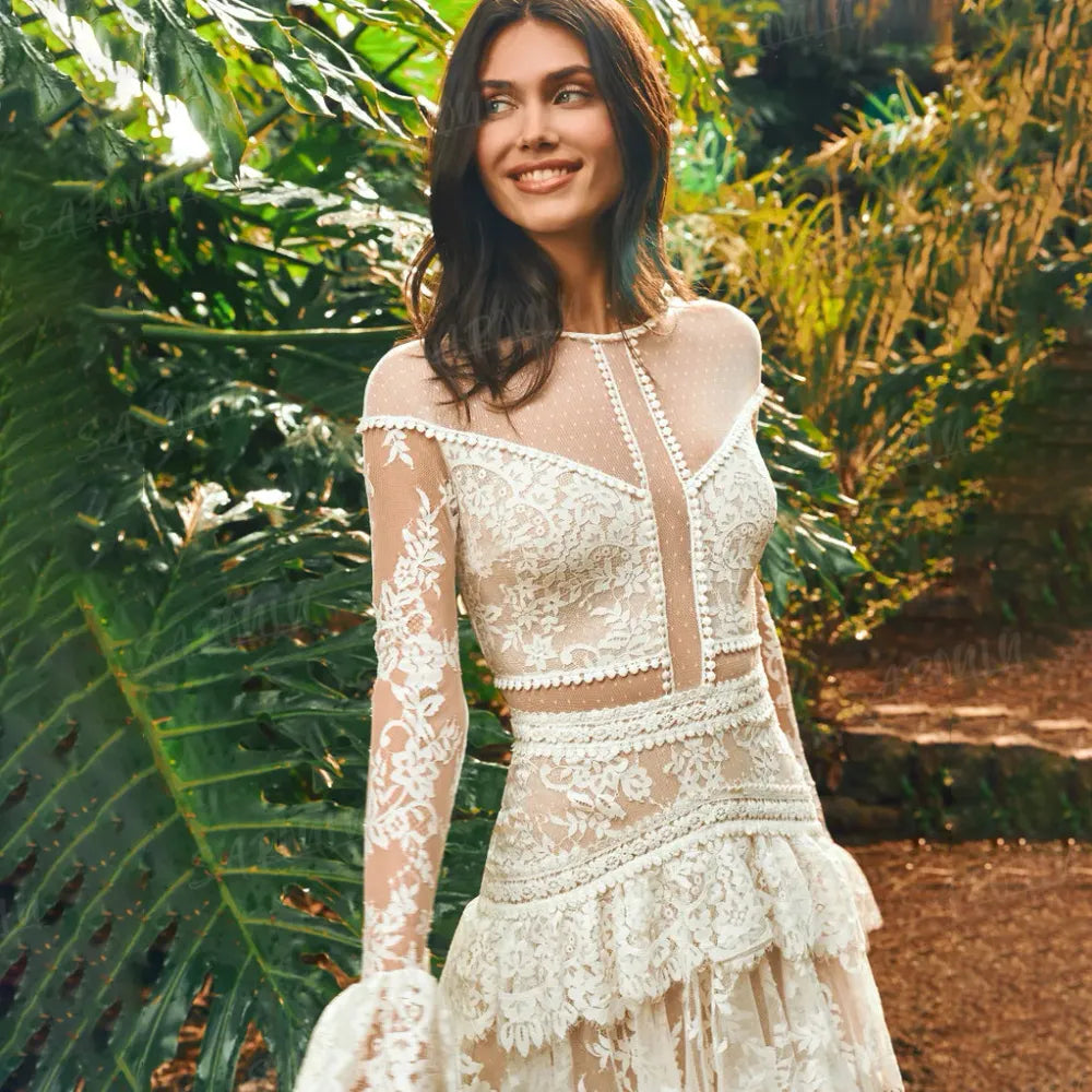 The Mila Dress is a one-of-a-kind Bohemian Lace Tulle Wedding Dress, perfect for the free-spirited bride. Made with custom tiers and long lace sleeves, this A-line dress features a backless design for a stunning and unique look. Step down the aisle in style with this beautiful and elegant bridal gown.
