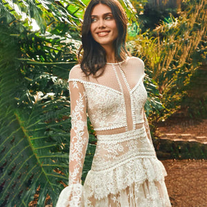 The Mila Dress is a one-of-a-kind Bohemian Lace Tulle Wedding Dress, perfect for the free-spirited bride. Made with custom tiers and long lace sleeves, this A-line dress features a backless design for a stunning and unique look. Step down the aisle in style with this beautiful and elegant bridal gown.