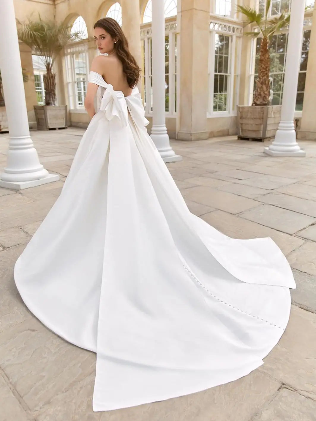 This 2-in-1 wedding dress offers versatility and style for a bride on her special day. It features a detachable ball gown with an off-shoulder design and a long, sheer tail for a dramatic entrance. The pleated bodice adds a touch of elegance and glamour, making it the perfect dress for any bride.