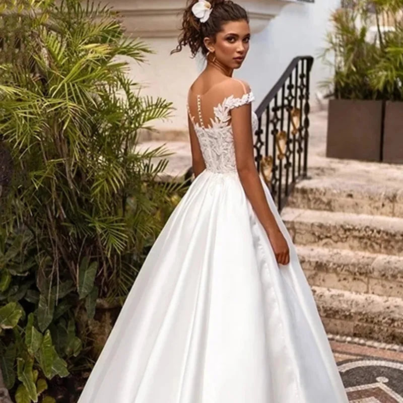 Elevate your wedding day look with the Robe Joanne. Featuring delicate lace appliques, modern satin fabric, and elegant cap sleeves, this dress offers a timeless and sophisticated style for any bride. Say "I do" in comfort and confidence with this stunning and versatile wedding dress.