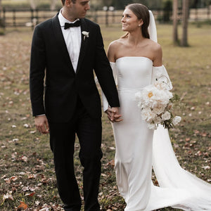 Introducing the Robe Eglantine, a minimalist wedding dress that exudes effortless elegance. This ivory crepe gown features detachable long sleeves for versatility and a sleek sheath silhouette with a brush train for a modern touch. The strapless design and buttons closure add convenience for the bride.