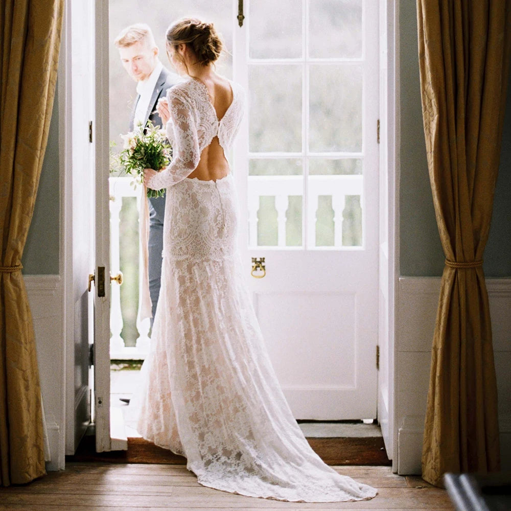 "Feel like a goddess on your special day with the Robe Ismay. This custom-made bridal gown features long lace sleeves, an open back with cutout detailing, and an illusion boat neck. The flowing chapel train and bohemian mermaid style add a touch of whimsy and romance. Say yes to the dress of your dreams!"