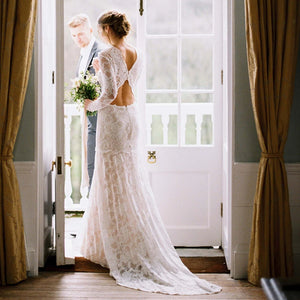 "Feel like a goddess on your special day with the Robe Ismay. This custom-made bridal gown features long lace sleeves, an open back with cutout detailing, and an illusion boat neck. The flowing chapel train and bohemian mermaid style add a touch of whimsy and romance. Say yes to the dress of your dreams!"