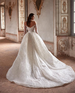 Indulge in luxury with the Robe Suzette. This elegant A-line wedding dress features an illusion neck, long sleeves, and intricate beading and pearls. Graceful and sophisticated, it's perfect for the modern bride. Complete your look with this designer gown and feel confident and stunning on your special day.
