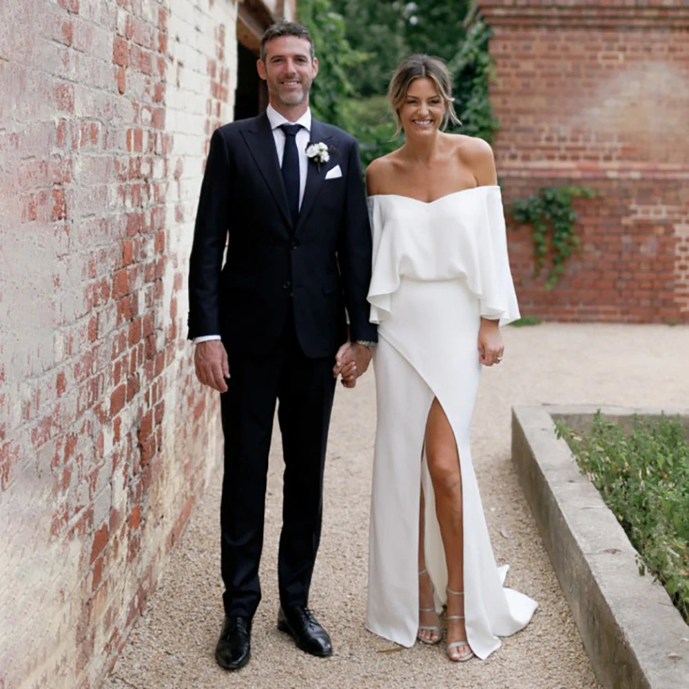 Look red-carpet ready in the captivating Sigourney robe. Featuring off-shoulder cape sleeves, a vintage crepe bodice, and a bias split open back with buttons, this gown makes an unforgettable statement. Custom made with an oversized cinched waist, take risks and be your own style icon on your big day.