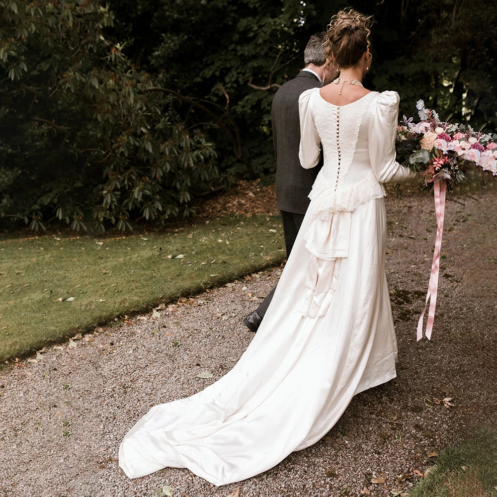This vintage bridal gown is a dream come true! With retro long bishop sleeves, delicate lace ruffles, custom-made closed back, and romantic Victorian style, you'll turn heads at your special day like a real-life bijou!