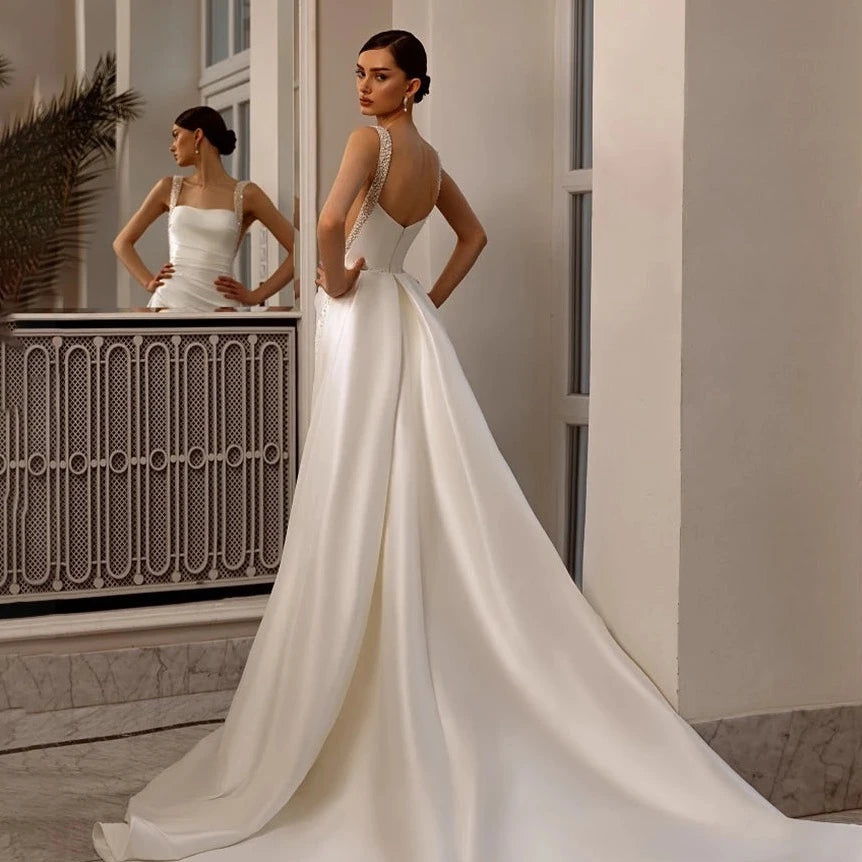 Indulge in luxury with our Robe Angeline. This bridal gown features a square neckline and elegant beading, perfectly complimented by a removable train. The custom cutouts and backless design add a touch of sophistication. Make a memorable entrance on your special day with the Robe Angeline.