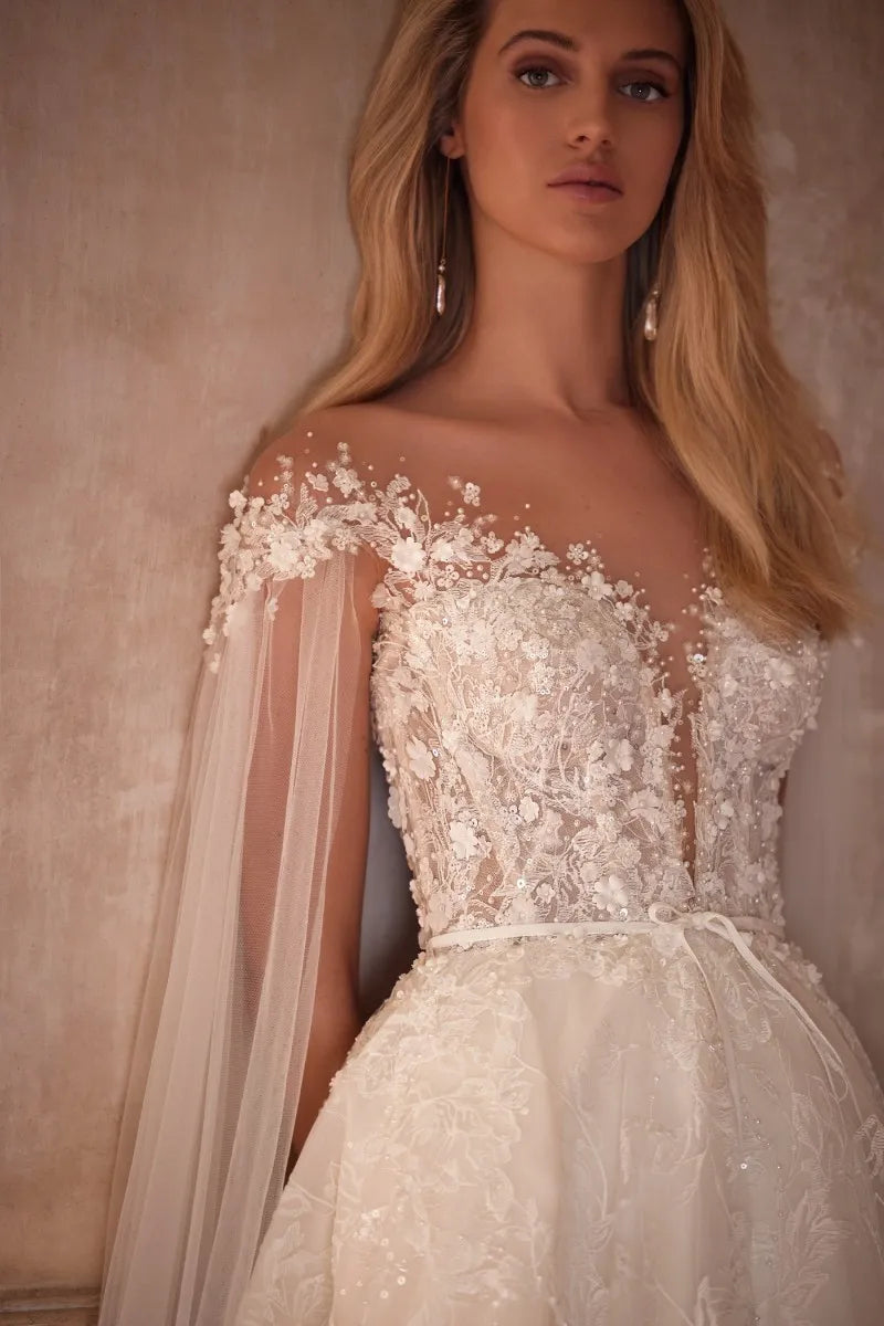 Elevate your wedding day look with our Dress Chantalle! Featuring a classic A-line silhouette, scoop neckline, and detachable cape sleeves, this dress is the epitome of elegance. Delicate appliques lace and a sophisticated train add romantic details to this modern bride gown. Make your special day unforgettable with Robe Chantalle.