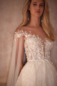 Elevate your wedding day look with our Dress Chantalle! Featuring a classic A-line silhouette, scoop neckline, and detachable cape sleeves, this dress is the epitome of elegance. Delicate appliques lace and a sophisticated train add romantic details to this modern bride gown. Make your special day unforgettable with Robe Chantalle.