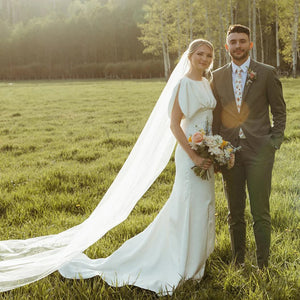 Elegant and modern, the Robe Bibi is the perfect choice for a bride looking to make a statement on her special day. With its empire waist, satin and pearl detailing, and backless design, this knee-length dress exudes both sophistication and simplicity. The slim slouch top and crepe bodycon silhouette create a figure-flattering look, perfect for a rustic or outdoor wedding.