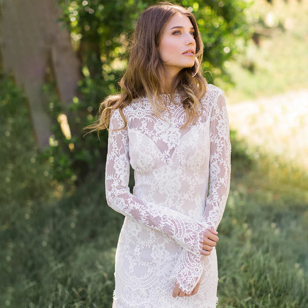 "Feel like a goddess on your special day with the Robe Ismay. This custom-made bridal gown features long lace sleeves, an open back with cutout detailing, and an illusion boat neck. The flowing chapel train and bohemian mermaid style add a touch of whimsy and romance. Say yes to the dress of your dreams!"