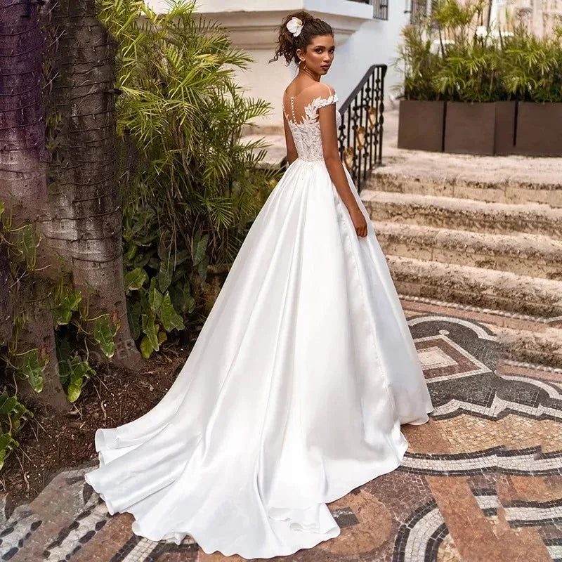 Elevate your wedding day look with the Robe Joanne. Featuring delicate lace appliques, modern satin fabric, and elegant cap sleeves, this dress offers a timeless and sophisticated style for any bride. Say "I do" in comfort and confidence with this stunning and versatile wedding dress.