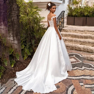 Elevate your wedding day look with the Robe Joanne. Featuring delicate lace appliques, modern satin fabric, and elegant cap sleeves, this dress offers a timeless and sophisticated style for any bride. Say "I do" in comfort and confidence with this stunning and versatile wedding dress.