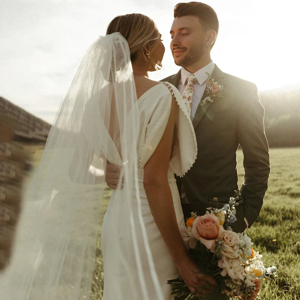 Elegant and modern, the Robe Bibi is the perfect choice for a bride looking to make a statement on her special day. With its empire waist, satin and pearl detailing, and backless design, this knee-length dress exudes both sophistication and simplicity. The slim slouch top and crepe bodycon silhouette create a figure-flattering look, perfect for a rustic or outdoor wedding.