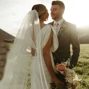 Elegant and modern, the Robe Bibi is the perfect choice for a bride looking to make a statement on her special day. With its empire waist, satin and pearl detailing, and backless design, this knee-length dress exudes both sophistication and simplicity. The slim slouch top and crepe bodycon silhouette create a figure-flattering look, perfect for a rustic or outdoor wedding.