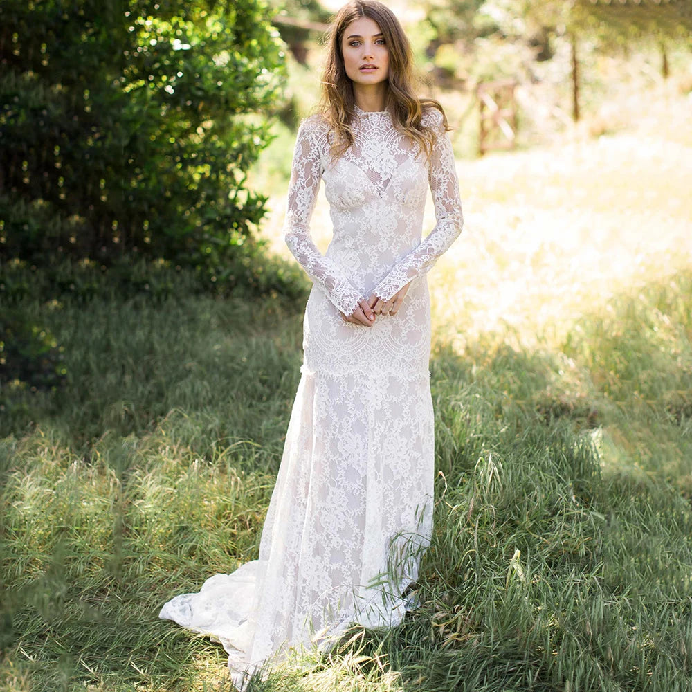 "Feel like a goddess on your special day with the Robe Ismay. This custom-made bridal gown features long lace sleeves, an open back with cutout detailing, and an illusion boat neck. The flowing chapel train and bohemian mermaid style add a touch of whimsy and romance. Say yes to the dress of your dreams!"