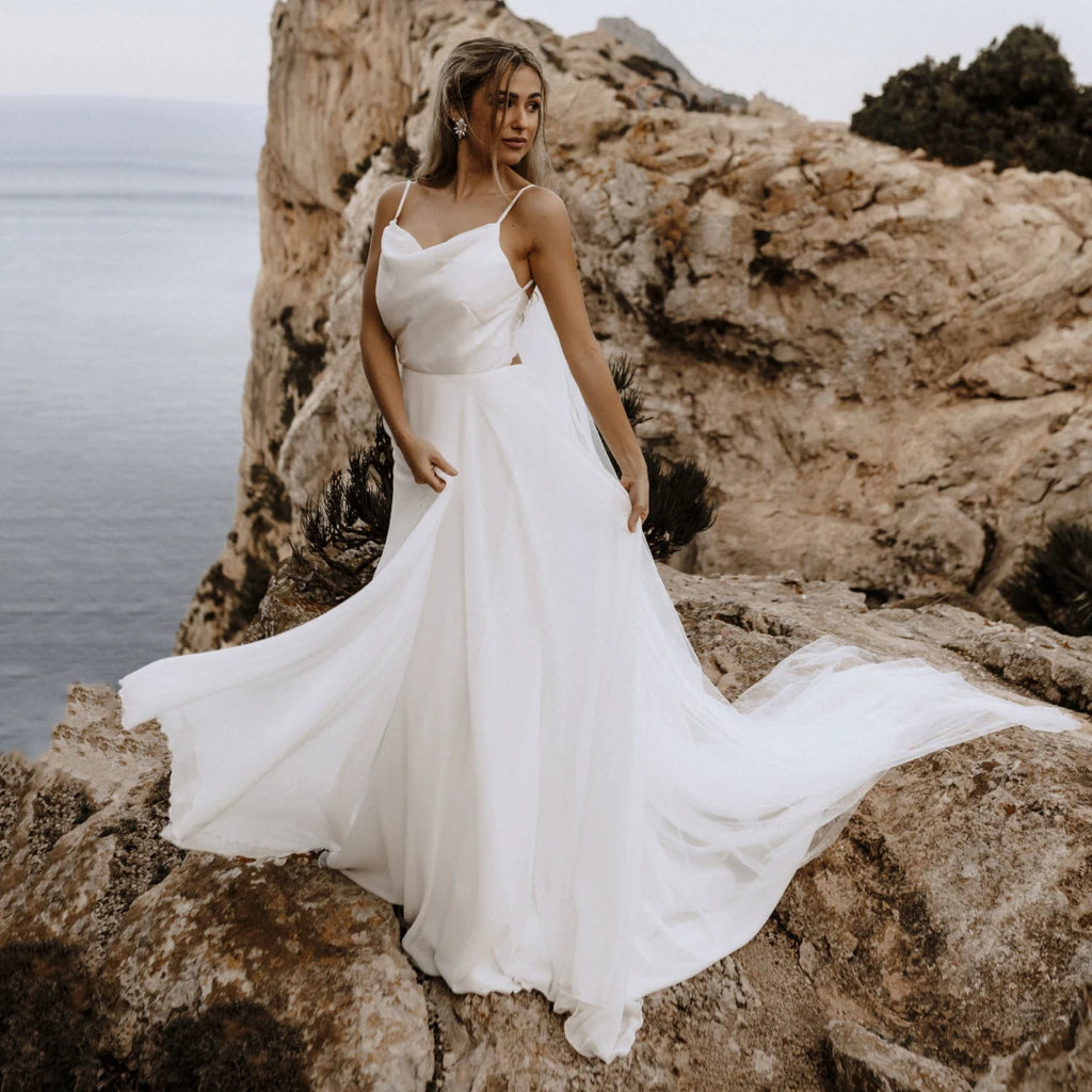 Let the perfect wedding gown inspire you with its sleek femininity! Our Robe Carolina features a spaghetti strap draped neckline, custom made brush train, ribbon tie backless, and a beach flowy silhouette. Crafted from luxurious silk chiffon, this bridal gown is perfect for a memorable day!