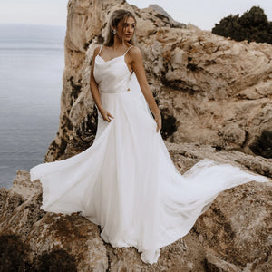 Let the perfect wedding gown inspire you with its sleek femininity! Our Robe Carolina features a spaghetti strap draped neckline, custom made brush train, ribbon tie backless, and a beach flowy silhouette. Crafted from luxurious silk chiffon, this bridal gown is perfect for a memorable day!