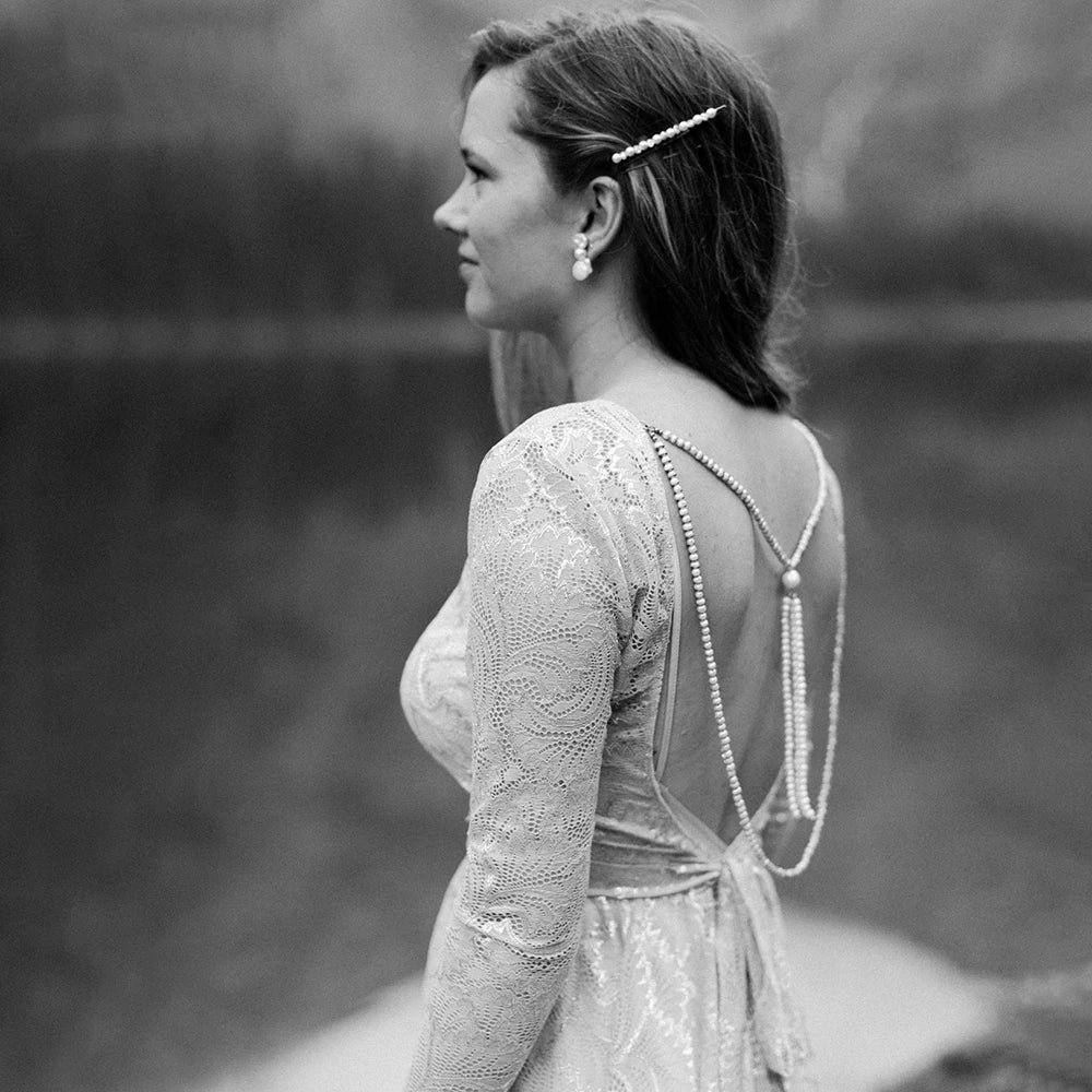 Experience the magic of your special day in our Dress Ava. The boho beach elopement design features long sleeves, a flare backless, and intricate lace with delicate pearls and tassels. The A-line silhouette and V-neckline are complemented by a custom-made belt for a perfect fit. Say "I do" in style with this unique and stunning bridal gown.
