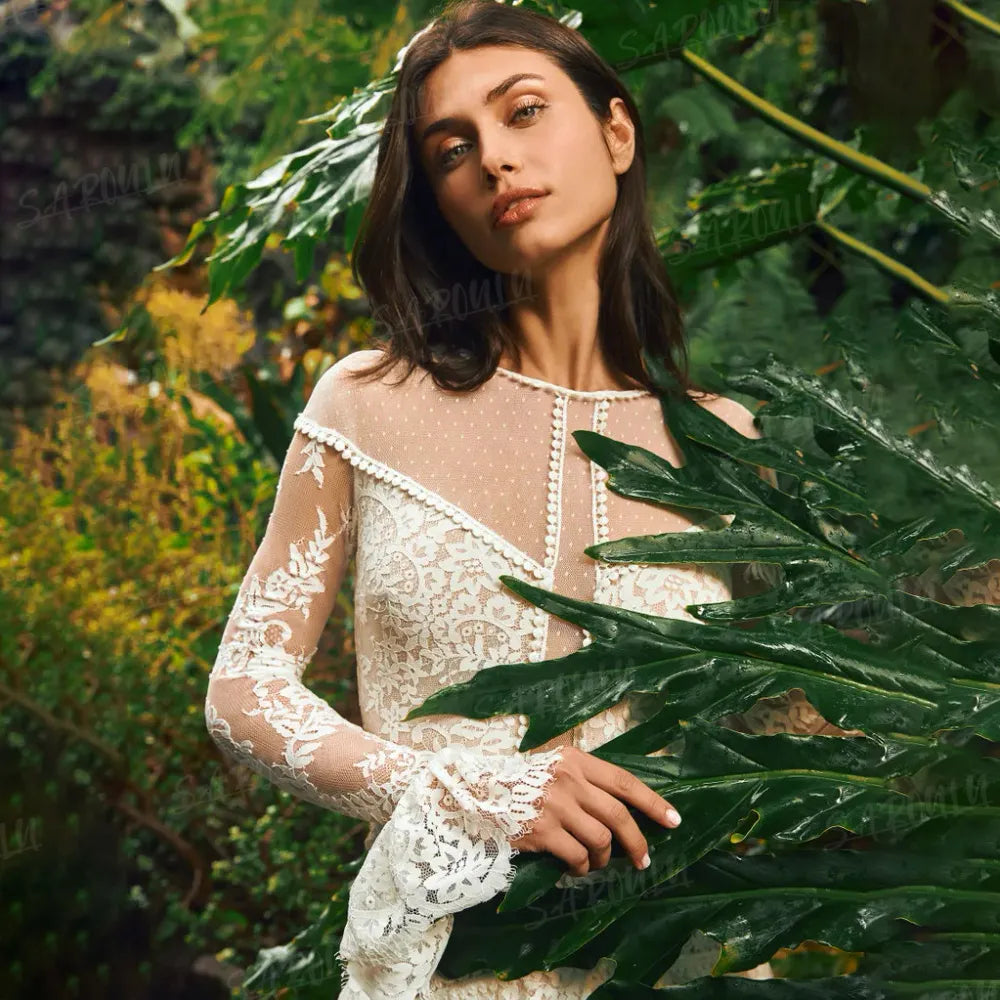 The Mila Dress is a one-of-a-kind Bohemian Lace Tulle Wedding Dress, perfect for the free-spirited bride. Made with custom tiers and long lace sleeves, this A-line dress features a backless design for a stunning and unique look. Step down the aisle in style with this beautiful and elegant bridal gown.