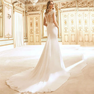 Get ready to stun on your special day with the Robe Avril. This elegant wedding dress features a flattering O-neckline and delicate cap sleeves, adorned with intricate lace appliques. The mermaid silhouette hugs your curves, allowing you to feel both sexy and sophisticated. Make a statement with the Robe Avril.