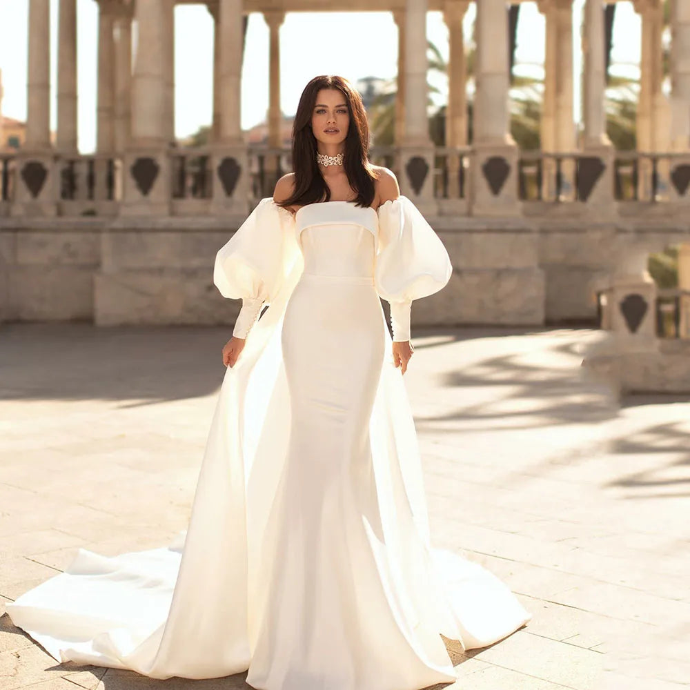 Experience the ultimate luxury with our beautifully crafted Robe Sandrine. Made with soft and silky satin, this wedding dress features a detachable train, perfect for a versatile and effortless look. The off the shoulder neckline and puff sleeves add a touch of romance and sophistication. Elevate your bridal experience with our Robe Sandrine.