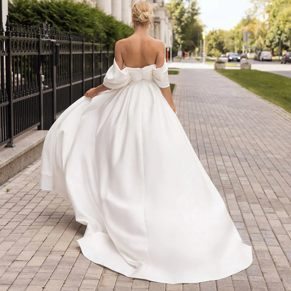Robe Amabel is an exquisite option for brides seeking an effortless and elegant look. Crafted from slinky fabric, it features an off-the-shoulder design, a mermaid silhouette with detachable train, a sweetheart neckline, and a backless side slit for an opulent and glamorous appeal. This luxurious robe will add an understated sophistication to any wedding look.