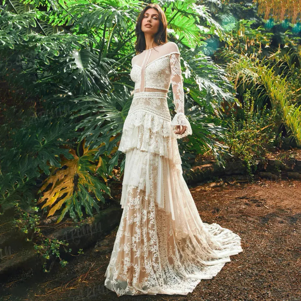 The Mila Dress is a one-of-a-kind Bohemian Lace Tulle Wedding Dress, perfect for the free-spirited bride. Made with custom tiers and long lace sleeves, this A-line dress features a backless design for a stunning and unique look. Step down the aisle in style with this beautiful and elegant bridal gown.