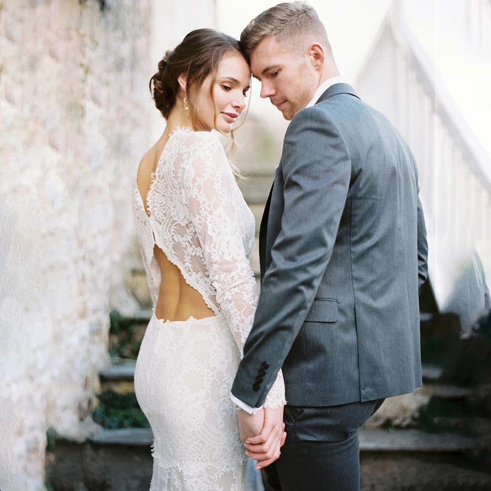 "Feel like a goddess on your special day with the Robe Ismay. This custom-made bridal gown features long lace sleeves, an open back with cutout detailing, and an illusion boat neck. The flowing chapel train and bohemian mermaid style add a touch of whimsy and romance. Say yes to the dress of your dreams!"