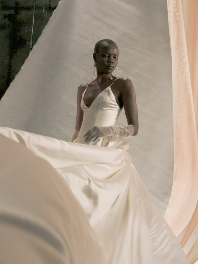 The Nina Gown epitomizes bridal elegance with its dramatic silhouette and meticulous construction. The plunging V neckline draws the eye upward, while the boned, self-lined bodice provides exceptional support and a refined shape. An elongated basque waist creates a flattering line, enhanced by strategic darts for a personalized fit. The voluminous skirt features a can-can ruffle at the hip for architectural structure and movement, culminating in an exaggerated cathedral train. 