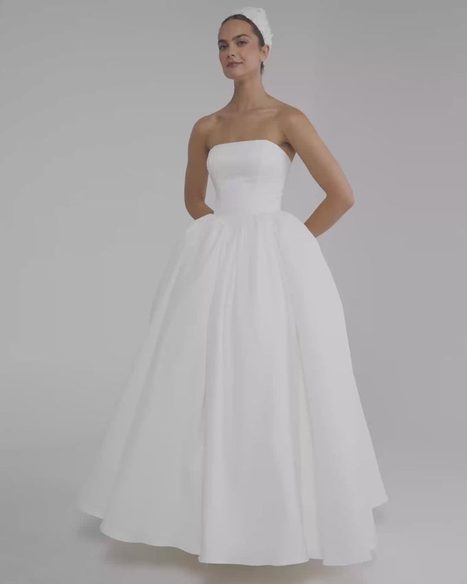Ivory satin short gown with A-line silhouette that combines timeless elegance and romantic charm. Strapless neckline fitted at the front, minimalist and retro design that flatters the figure. Perfect for brides seeking a simple yet captivating look. Includes matching veil sold separately. Ideal for intimate ceremonies, civil weddings, or special celebrations where understated sophistication takes center stage.