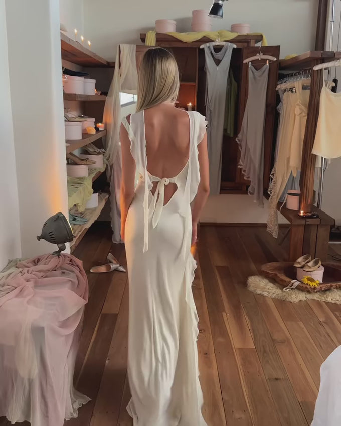 The Silk Blend Ivory Maxi Dress combines refined elegance with everyday comfort. Crafted from medium-weight jersey fabric, it molds gracefully to your form while allowing unrestricted movement. The adjustable tie-back closure lets you customize the fit, while delicate ruffled edges add flowing dimension. A detachable scarf accent provides styling versatility for any occasion. Unlined construction ensures breathability and ease, making this piece perfect for weddings, celebrations, or whenever you want to lo