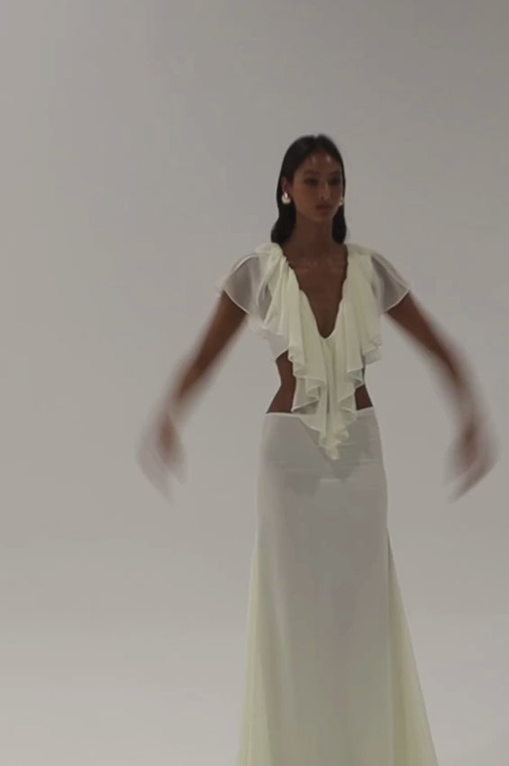 Discover timeless elegance with the Darling Set in Ivory, a refined two-piece collection designed for modern sophistication. The low-rise maxi skirt features a sleek, elongated silhouette with a delicate fluted hem that flows gracefully, while a concealed side zipper preserves a polished silhouette. The coordinating top showcases an elegant v-neckline adorned with cascading ruffles that drape beautifully across the shoulders, secured with a tie closure. 